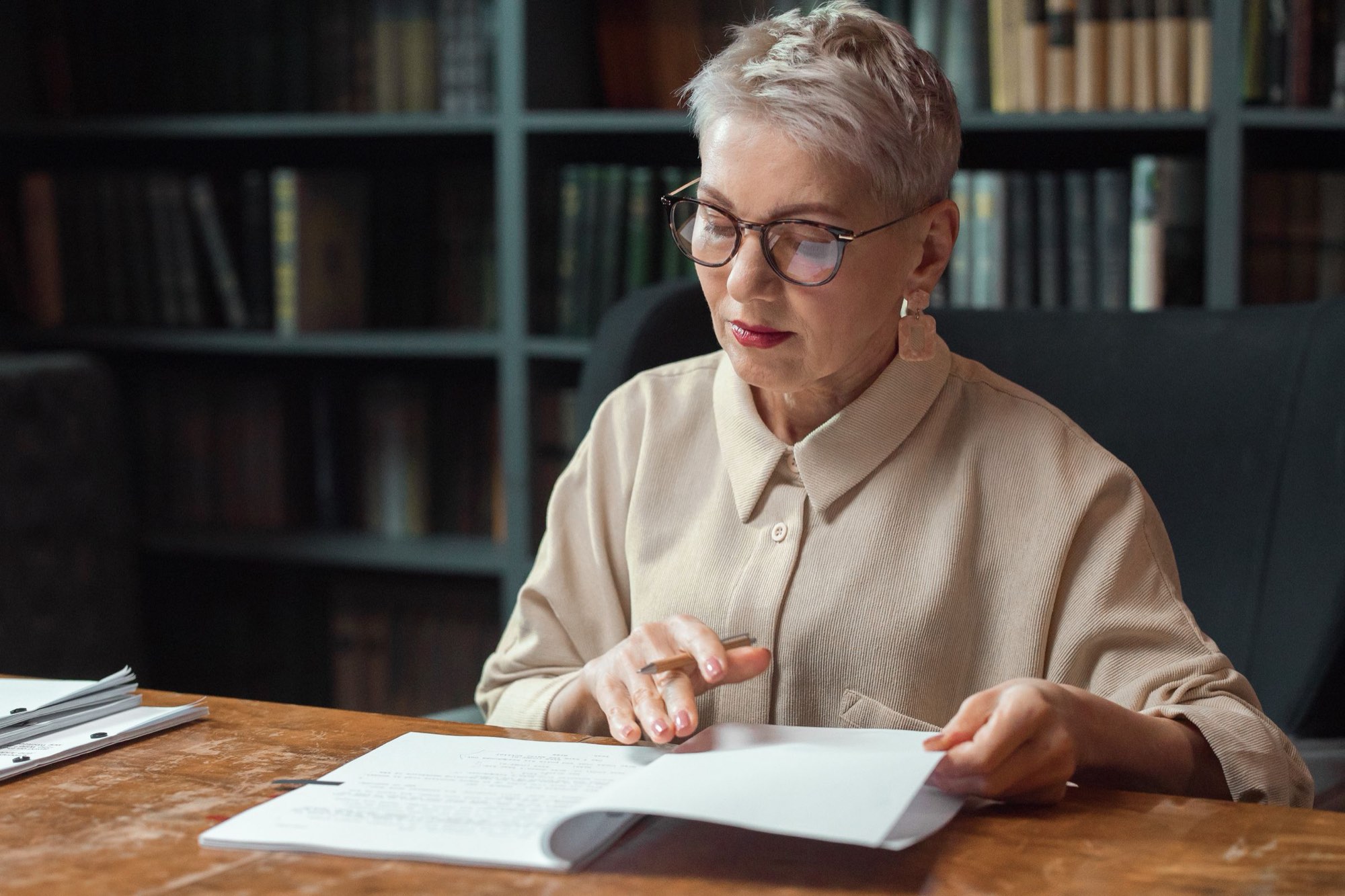 A senior researcher reading a bound manuscript at a wooden desk, pencil in hand